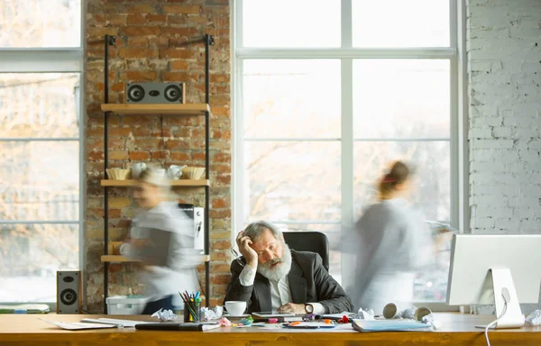 Нервовий і втомлений бос на своєму робочому місці зайнятий, поки люди рухаються поблизу розмитих — стокове фото