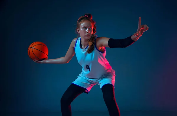 Joven jugador de baloncesto femenino caucásico en fondo estudio azul en luz de neón — Foto de Stock