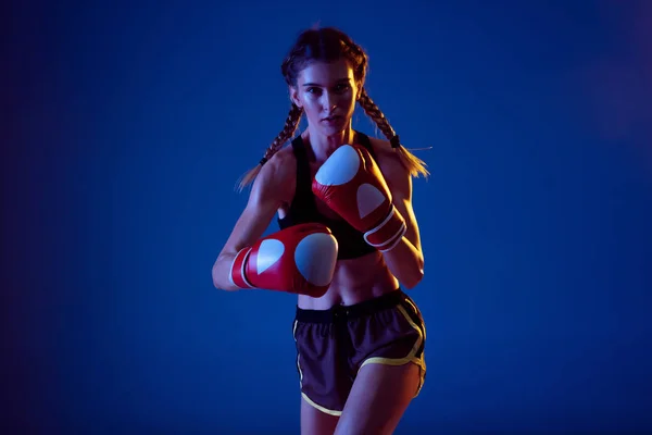 Fit mulher caucasiana em sportswear boxe em fundo estúdio azul em luz de néon — Fotografia de Stock