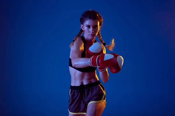 Подходит кавказка в спортивном боксе на синем студийном фоне в неоновом свете — стоковое фото