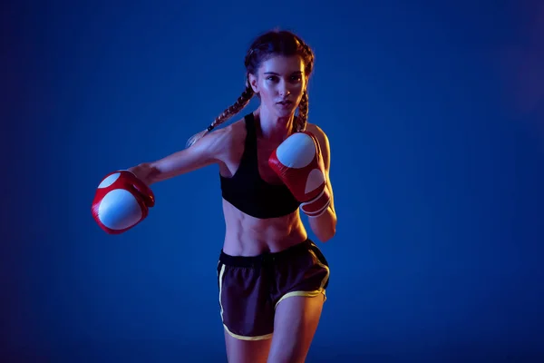 Fit caucasian woman in sportswear boxing on blue studio background in neon light — ストック写真