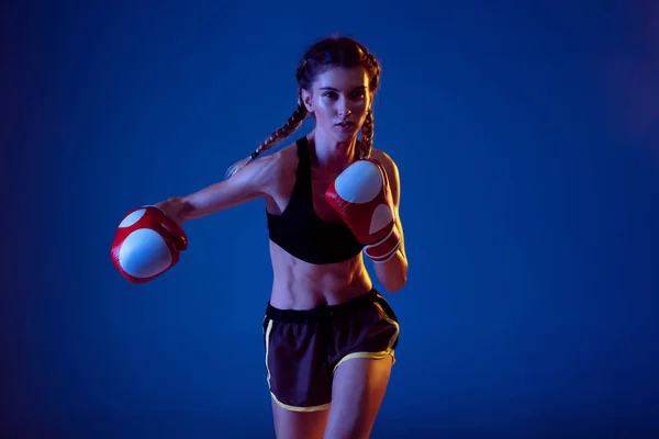 Fit mulher caucasiana em sportswear boxe em fundo estúdio azul em luz de néon — Fotografia de Stock