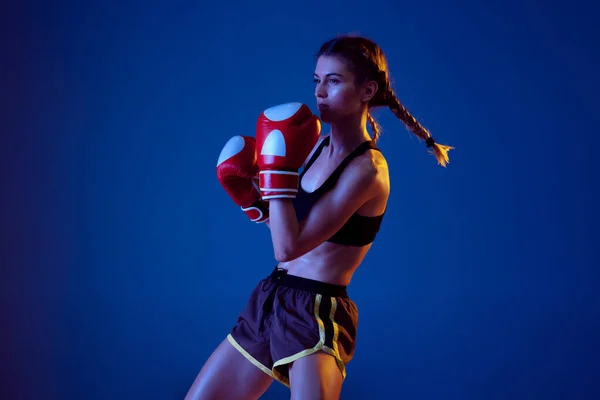 Fit mulher caucasiana em sportswear boxe em fundo estúdio azul em luz de néon — Fotografia de Stock