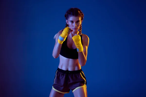 Fit caucasian woman in sportswear boxing on blue studio background in neon light — Stock Photo, Image