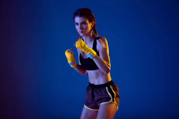 Fit caucasian woman in sportswear boxing on blue studio background in neon light — Stock Photo, Image