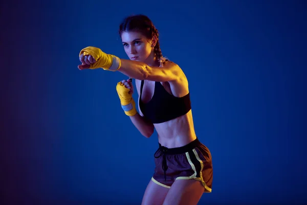 Fit biały kobieta w sportowy odzież boks na niebieski studio tło w neon światło — Zdjęcie stockowe
