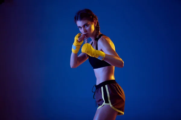 Fit caucasian woman in sportswear boxing on blue studio background in neon light — Stock Photo, Image