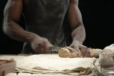Afro-Amerikalı bir adam mutfak bıçağıyla taze ekmek dilimliyor.