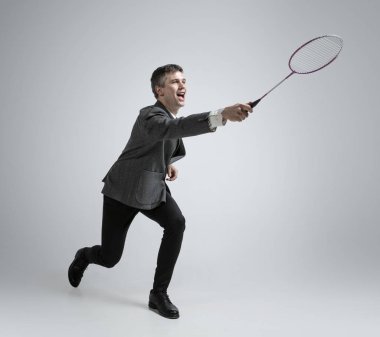 Caucasian man in office clothes plays badminton isolated on grey studio background clipart