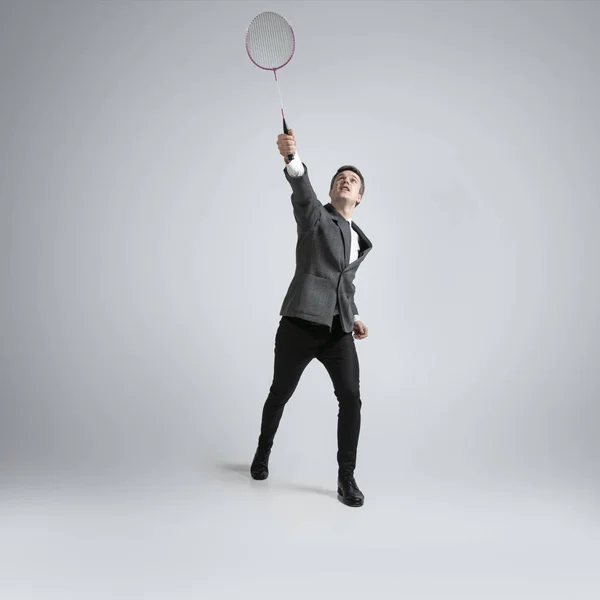 Blanke man in kantoor kleding speelt badminton geïsoleerd op grijze studio achtergrond — Stockfoto