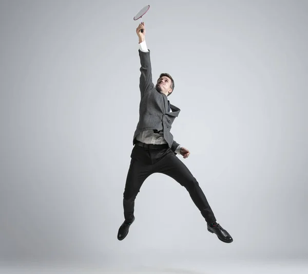 Blanke man in kantoor kleding speelt badminton geïsoleerd op grijze studio achtergrond — Stockfoto