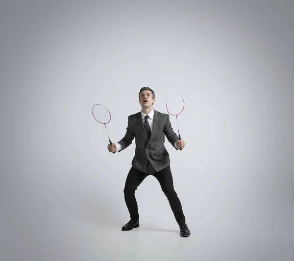 Uomo caucasico in abiti da ufficio gioca badminton isolato su sfondo grigio studio — Foto Stock