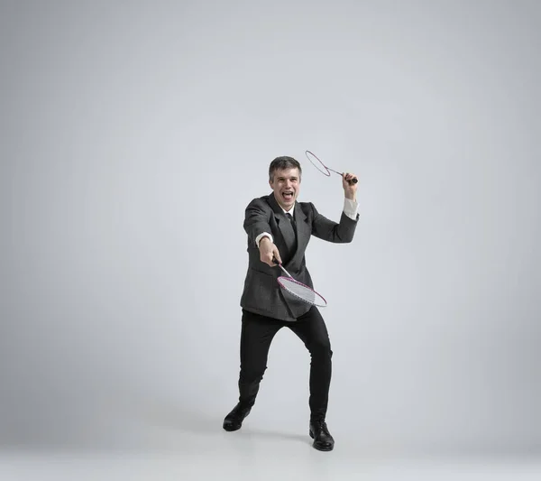 Uomo caucasico in abiti da ufficio gioca badminton isolato su sfondo grigio studio — Foto Stock