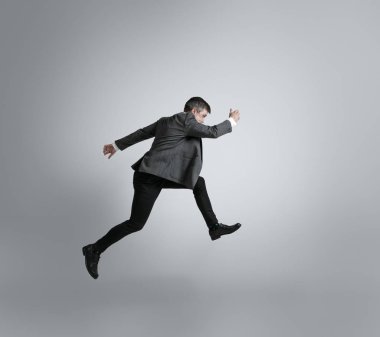 Caucasian man in office clothes running isolated on grey studio background clipart