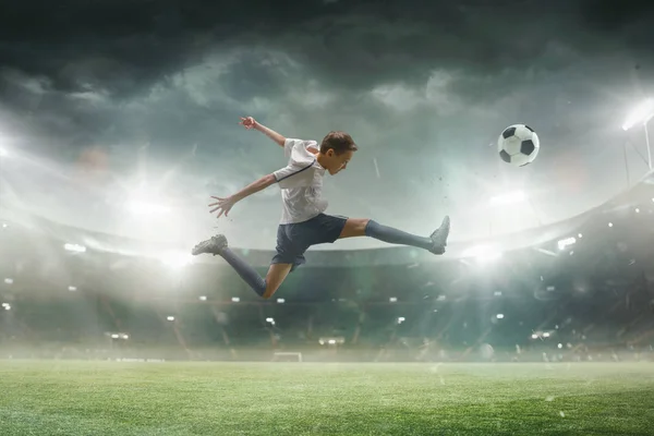Giovane giocatore di calcio maschile calci palla sullo stadio con torce elettriche sullo sfondo — Foto Stock