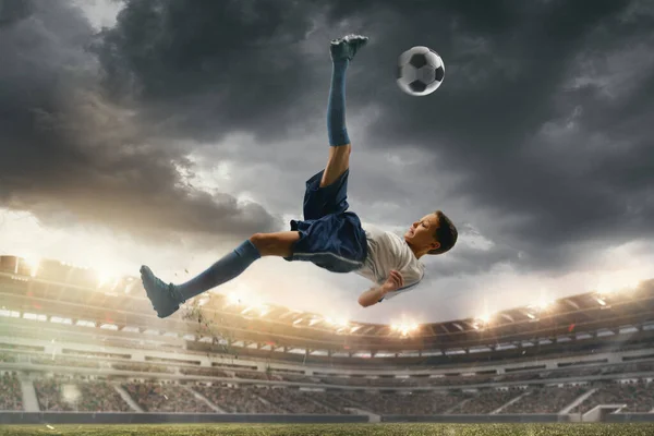 Joven jugador de fútbol masculino pateando pelota en el estadio con linternas en el fondo — Foto de Stock