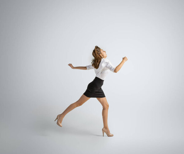 Caucasian woman in office clothes running isolated on grey studio background
