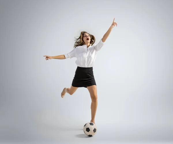 Caucasian woman in office clothes kicking ball isolated on grey studio background — Stock Photo, Image