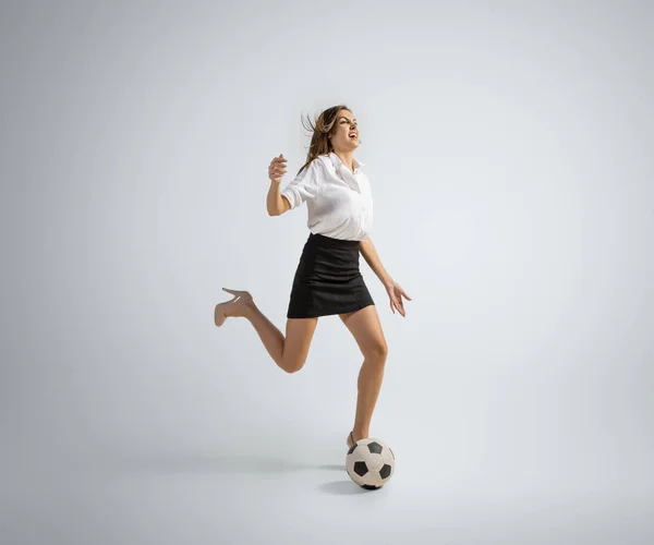 Kaukasische Frau in Bürokleidung kickt Ball isoliert auf grauem Studiohintergrund — Stockfoto