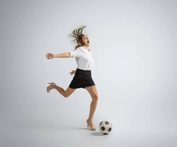 Caucasian woman in office clothes kicking ball isolated on grey studio background — Stock Photo, Image