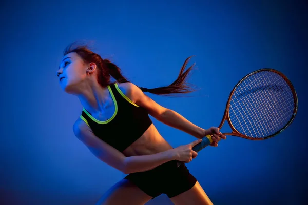 Little caucasian girl playing tennis isolated on blue background in neon light — ストック写真