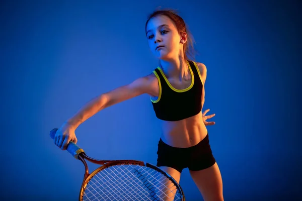 Little caucasian girl playing tennis isolated on blue background in neon light — Stock Photo, Image