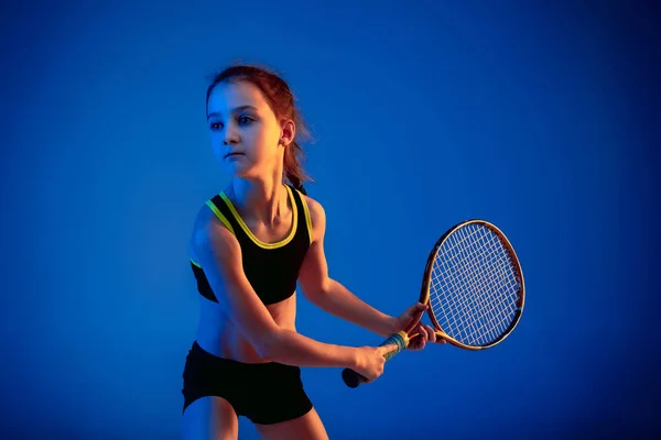 작은 백인 소녀가 네온 빛을 받으며 푸른 배경에서 고립된 채 테니스를 치는 모습 — 스톡 사진