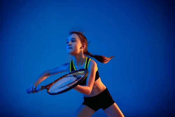 Little caucasian girl playing tennis isolated on blue background in neon light — ストック写真