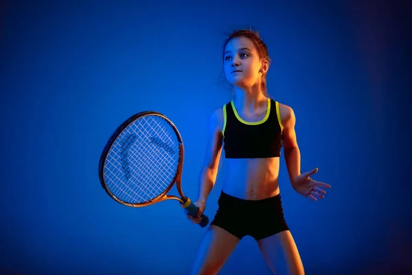 Маленькая кавказская девочка играет в теннис на голубом фоне в неоновом свете — стоковое фото