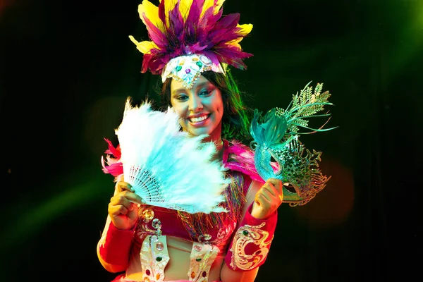 Beautiful young woman in carnival mask and masquerade costume in colorful lights