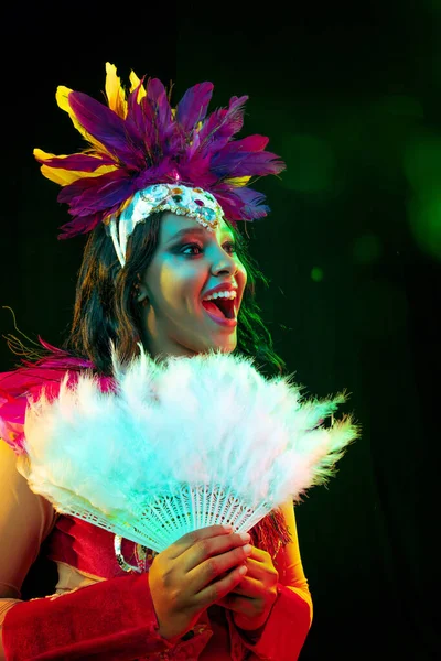 Mooie jonge vrouw in carnaval masker en maskerade kostuum in kleurrijke lichten — Stockfoto