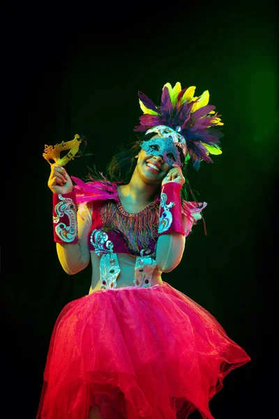 Hermosa mujer joven en máscara de carnaval y disfraz de mascarada en luces de colores — Foto de Stock