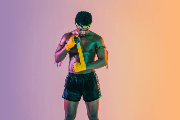 Muay thai. Young man exercising thai boxing on gradient background in neon light. Fighter practicing, training in martial arts in action, motion. Healthy lifestyle, sport, asian culture concept.
