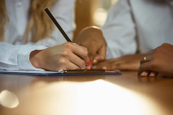 Close up of african-american and caucasian humans hands writing on sheets on wooden table