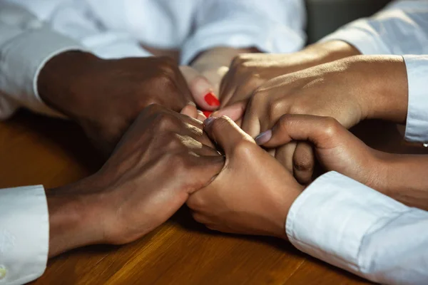 Primer plano de los seres humanos afroamericanos y caucásicos sosteniendo las manos sobre una mesa de madera — Foto de Stock