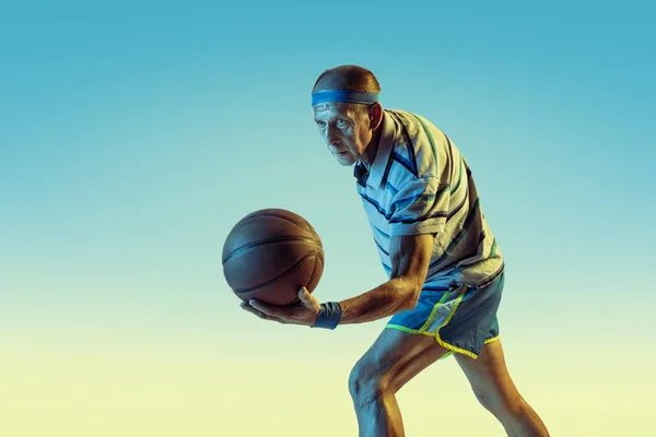 Senior-Mann spielt Basketball in Sportbekleidung auf Gradientenhintergrund und Neonlicht — Stockfoto