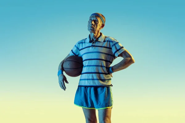 Старший чоловік грає в баскетбол у спортивному одязі на градієнтному фоні та неоновому світлі — стокове фото
