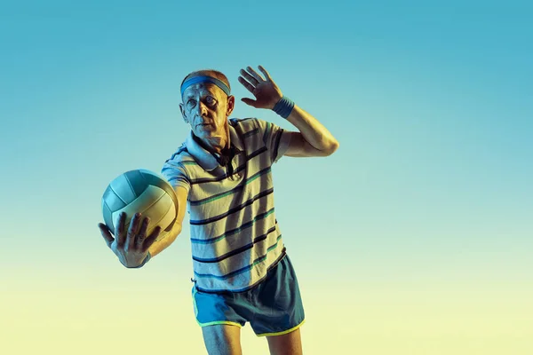 Senior man playing volleyball in sportwear on gradient background and neon light — Stock Photo, Image