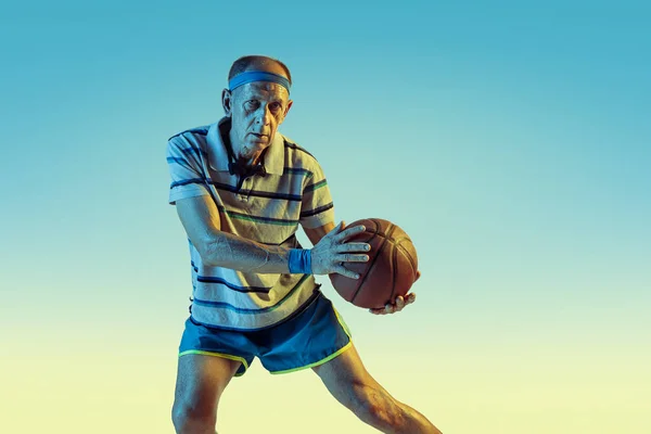 Hombre mayor jugando baloncesto en ropa deportiva sobre fondo degradado y luz de neón — Foto de Stock