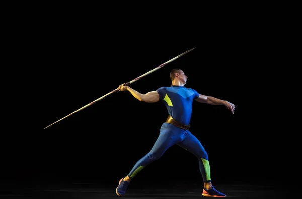 Male athlete practicing in throwing javelin isolated on black studio background in neon light