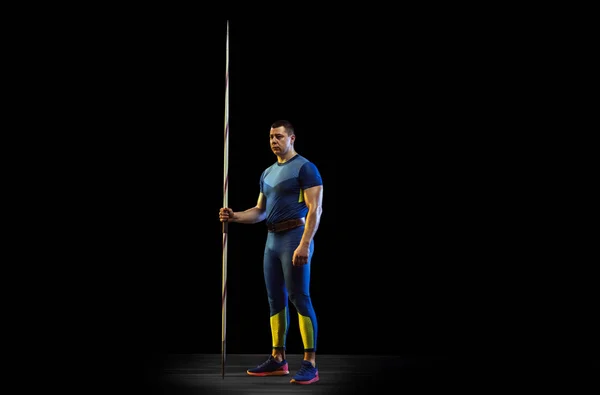 Atleta masculino practicando en lanzar jabalina aislada sobre fondo de estudio negro en luz de neón —  Fotos de Stock