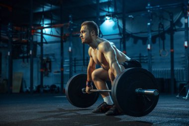 Spor salonunda ağırlık kaldırmada antrenman yapan beyaz bir adam.