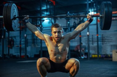 Spor salonunda ağırlık kaldırmada antrenman yapan beyaz bir adam.