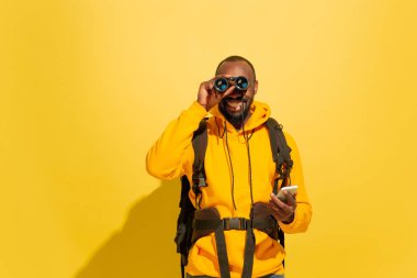 Sarı arka planda izole edilmiş neşeli Afrikalı genç bir turistin tam boy portresi.