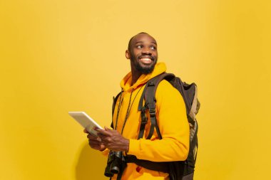 Sarı arka planda izole edilmiş neşeli Afrikalı genç bir turistin tam boy portresi.