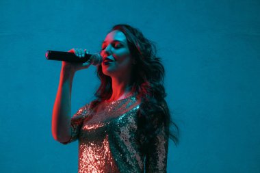 Caucasian female singer portrait isolated on blue studio background in neon light