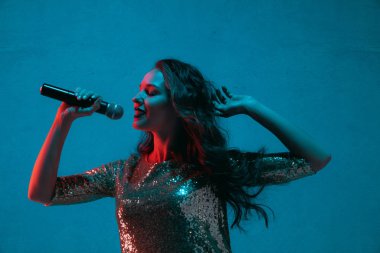 Caucasian female singer portrait isolated on blue studio background in neon light