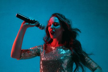 Caucasian female singer portrait isolated on blue studio background in neon light