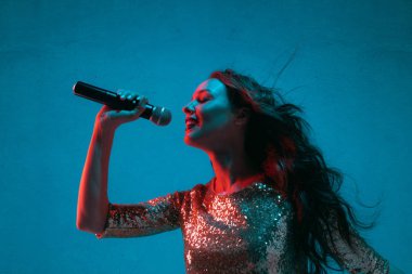 Caucasian female singer portrait isolated on blue studio background in neon light