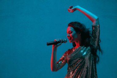 Caucasian female singer portrait isolated on blue studio background in neon light